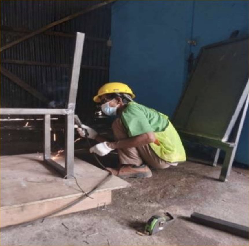Tukang las tim workshop Herkam Atelier mengerjakan rangka besi dengan helm dan masker